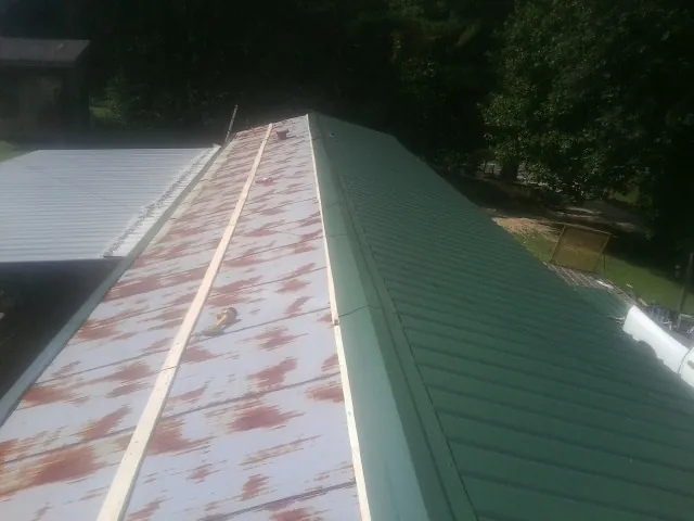 Old rusted panels beside newly installed green metal roofing — Wind Damage Roof Repair by Roofing Brothers in Seabrook
