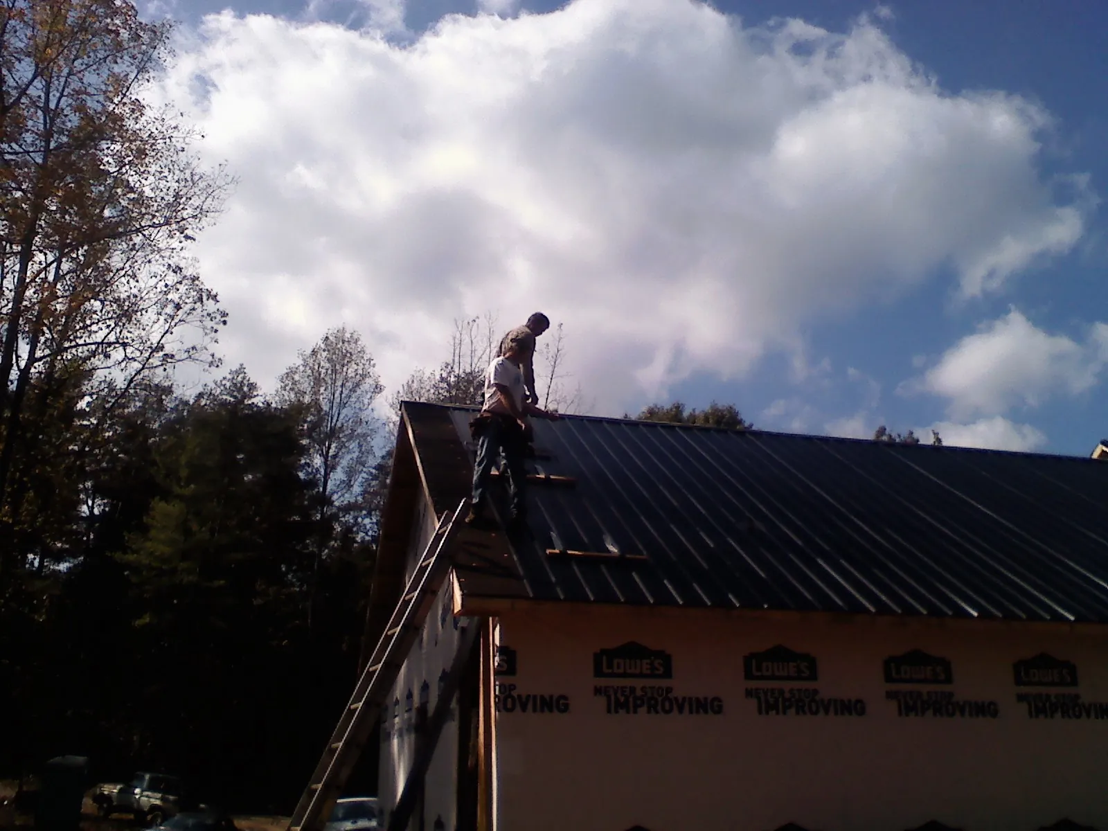 Roofer fastening dark metal panels high against a cloudy sky, from a Roof Inspection job in Seabrook