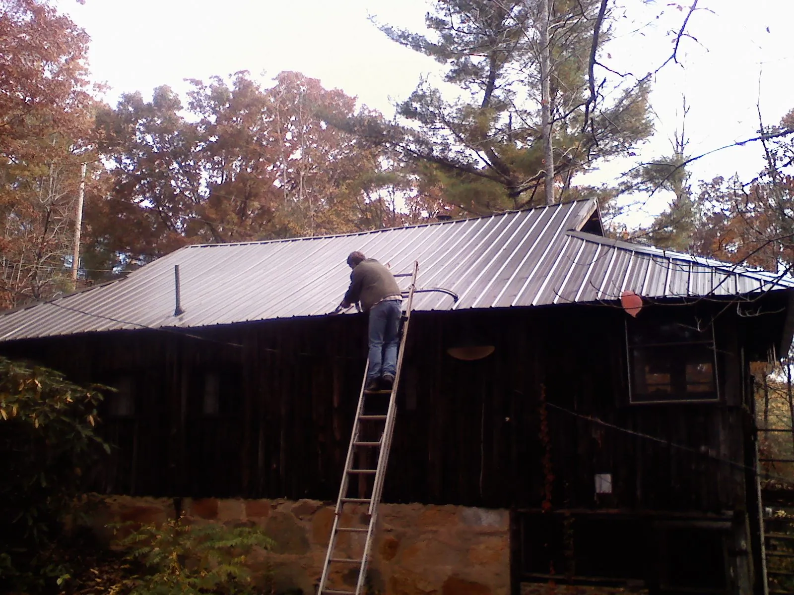 Roofer on a ladder working along the edge of a cabin metal roof in Seabrook