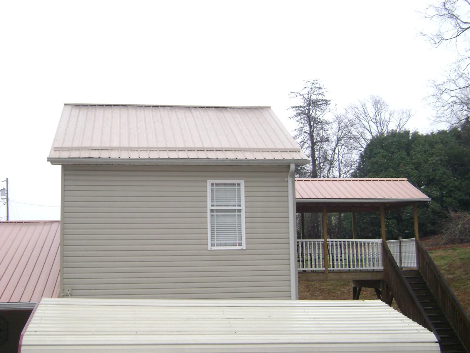 Tan metal roofs on a two story addition and attached porch, from a Roof Replacement job in Seabrook